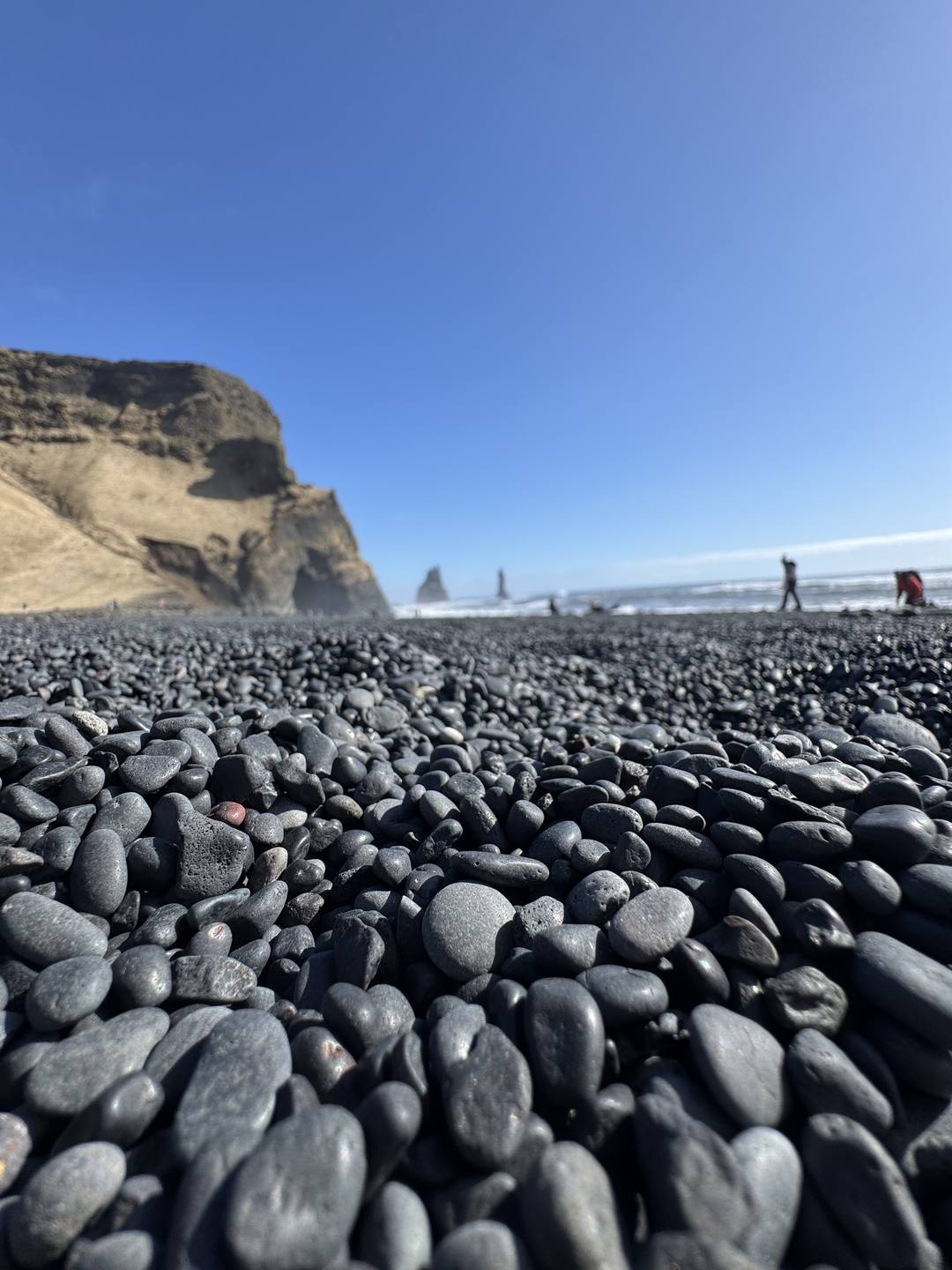 Rounded basalt pebbles and the Reynisdrangar sea stacks at Reynisfjara black sand beach, Iceland South Coast